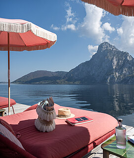 Liegen und rosa Sonnenschirme direkt am Traunsee mit Blick auf den Traunstein.