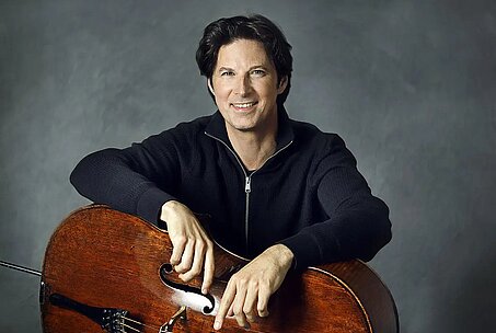 Daniel Müller-Schott sitzt mit seinem Cello vor einem dunklen Hintergrund.