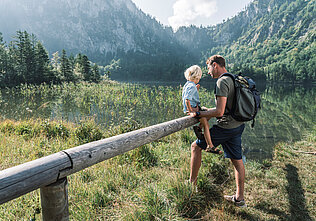 Ein Bub sitzt auf einem Holzgeländer beim Laudachsee in Grünberg, (c) Oberösterreich Tourismus/Traunsee-Almtal/Robert Maybach