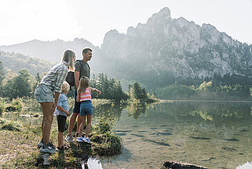 Eine Familie steht am Seeufer des Laudachsee in Grünberg im Salzkammergut und schaut aufs Wasser, die Berge spiegeln sich im See, (c) Oberösterreich Tourismus/Traunsee-Almtal/Robert Maybach