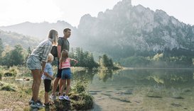 Eine Familie steht am Seeufer des Laudachsee in Grünberg im Salzkammergut und schaut aufs Wasser, die Berge spiegeln sich im See, (c) Oberösterreich Tourismus/Traunsee-Almtal/Robert Maybach
