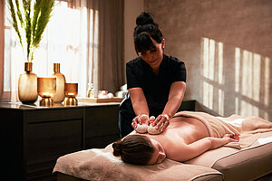 Spa-Behandlung mit Kräuterstempeln in ruhiger Wellnessatmosphäre.